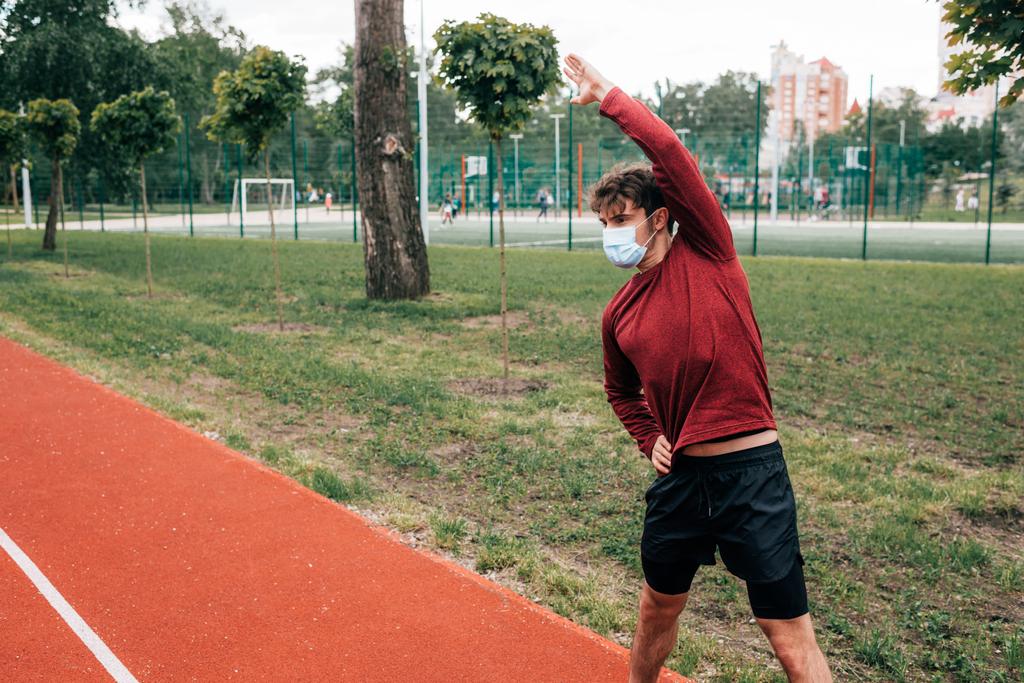 Deportista en máscara médica haciendo ejercicio en pista en el parque
  - Foto, Imagen