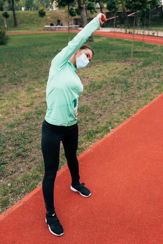 Junge Frau in medizinischer Maske trainiert auf Laufbahn im Park  - Foto, Bild