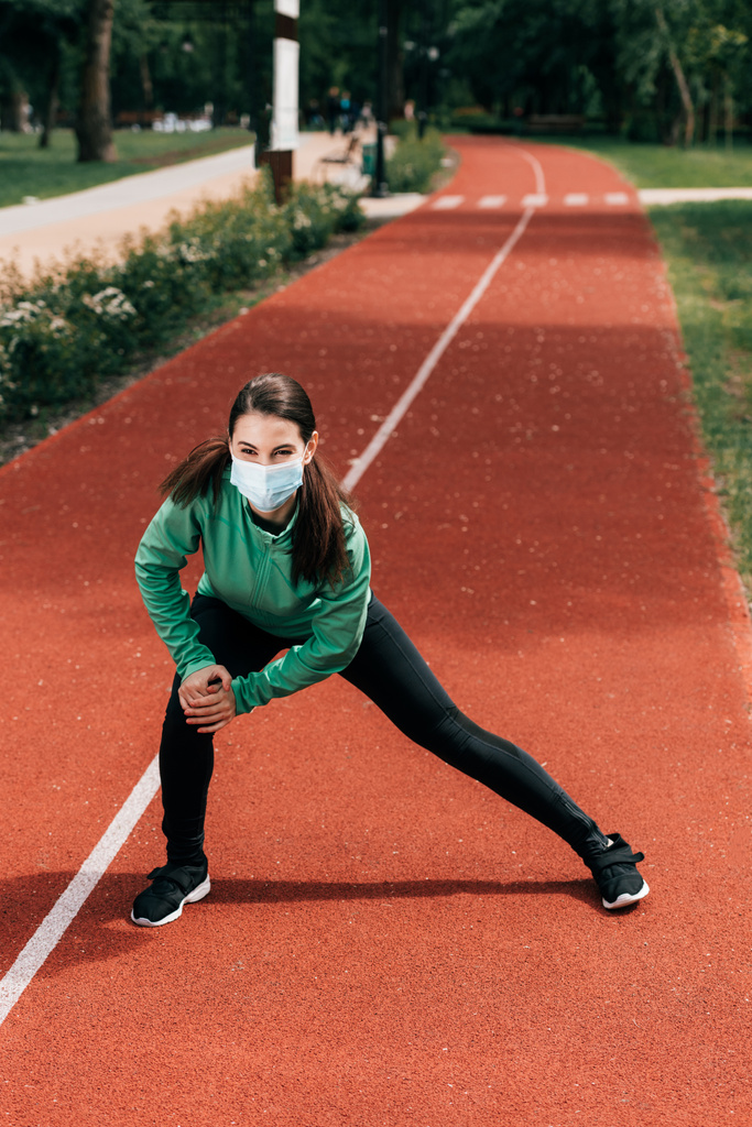 Sportlerin mit medizinischer Maske trainiert auf Laufbahn im Park  - Foto, Bild