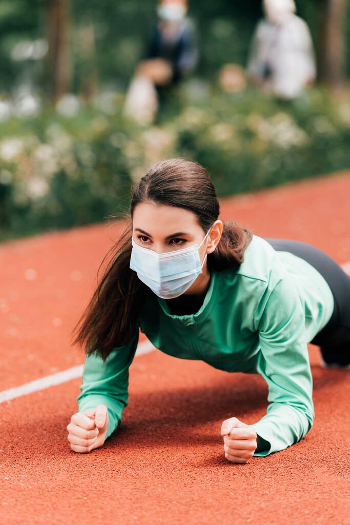 Jovem desportista em máscara médica fazendo prancha durante o treinamento no parque
  - Foto, Imagem