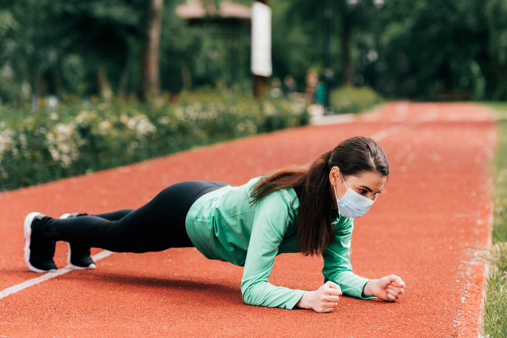 Oldalnézet sportos nő orvosi maszk csinál deszka edzés közben a parkban  - Fotó, kép