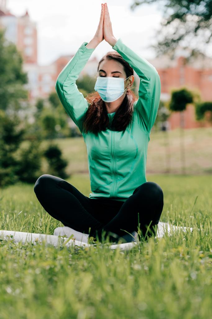 Szelektív fókusz nő orvosi maszk ül jóga póz fitness mat a parkban  - Fotó, kép
