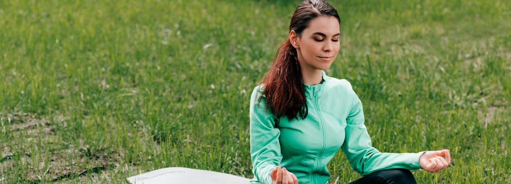 Junge Frau meditiert auf Fitnessmatte im Park  - Foto, Bild