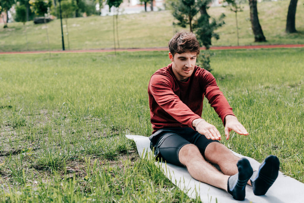 Przystojny sportowiec ocieplający się na macie fitness w parku  - Zdjęcie, obraz