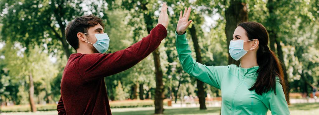 Horizontal image of sportsman in medical mask high five to girlfriend in park - Photo, Image