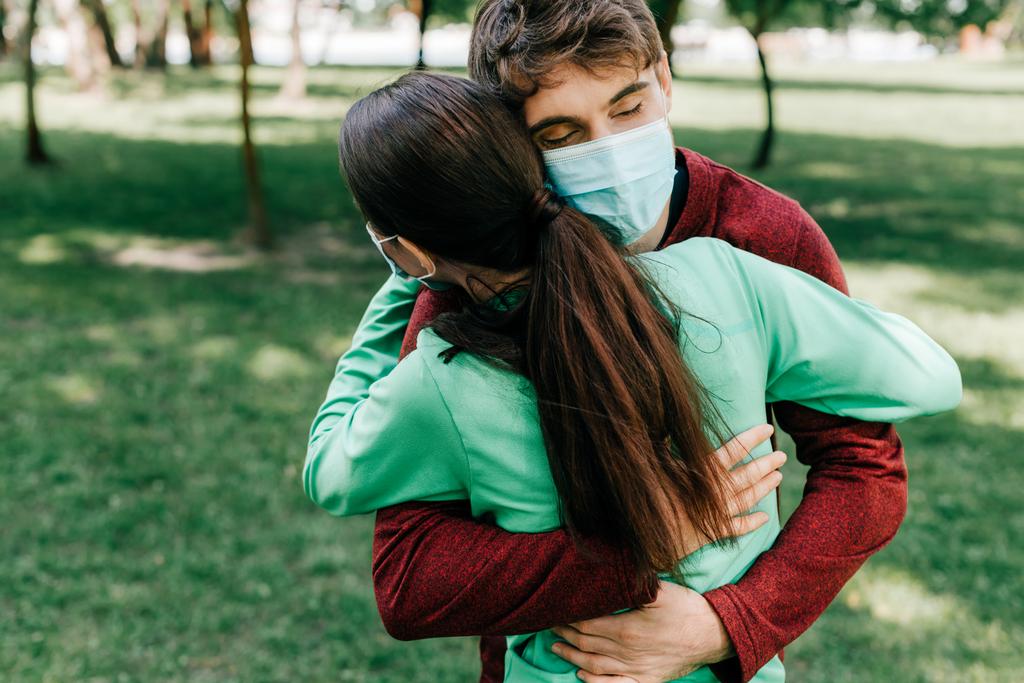 Sportsman in medical mask hugging sportswoman in park  - Photo, Image