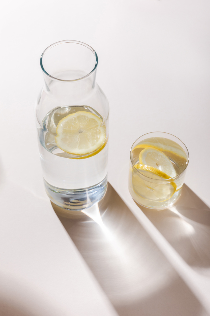 makeaa vettä sitruunaviipaleilla karahvi ja lasi valkoisella pöydällä varjoilla - Valokuva, kuva