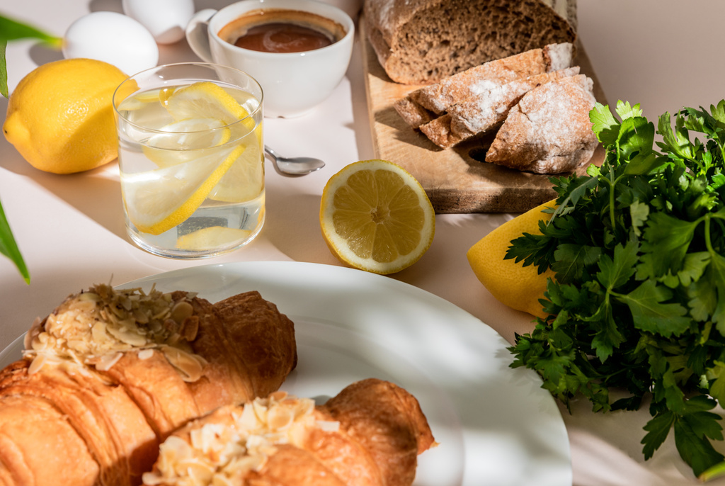 tuoreet croissantit, leipä, persilja, kahvi ja sitruunavesi aamiaiseksi harmaalla pöydällä, valikoiva keskittyminen - Valokuva, kuva