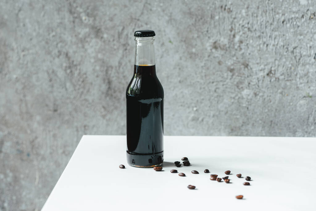 Kalter Brühkaffee in Flaschen neben Kaffeebohnen auf weißem Tisch - Foto, Bild