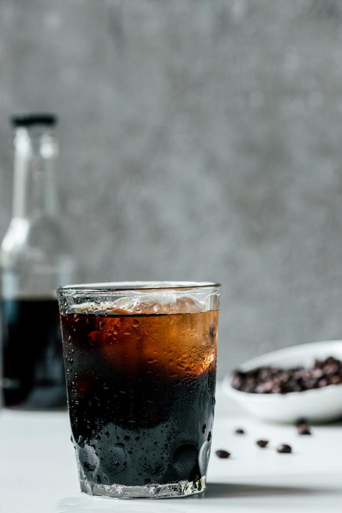 foyer sélectif de café infusé à froid avec de la glace dans le verre près de la bouteille et des grains de café sur la table blanche
 - Photo, image