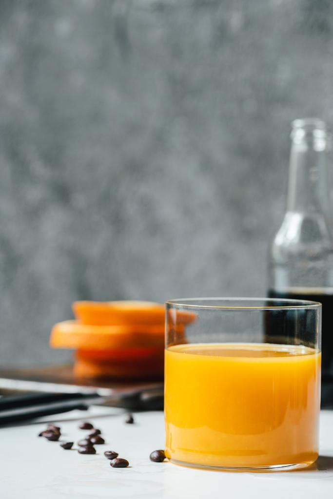 foco seletivo de suco de laranja em vidro perto de café de cerveja fria e grãos de café na mesa branca
 - Foto, Imagem