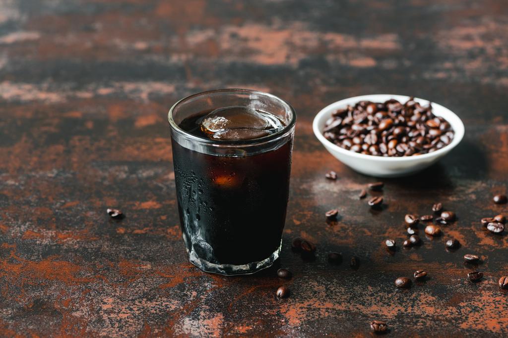selektivní zaměření studené kávy s ledem ve skle u kávových zrn na rezavém povrchu - Fotografie, Obrázek