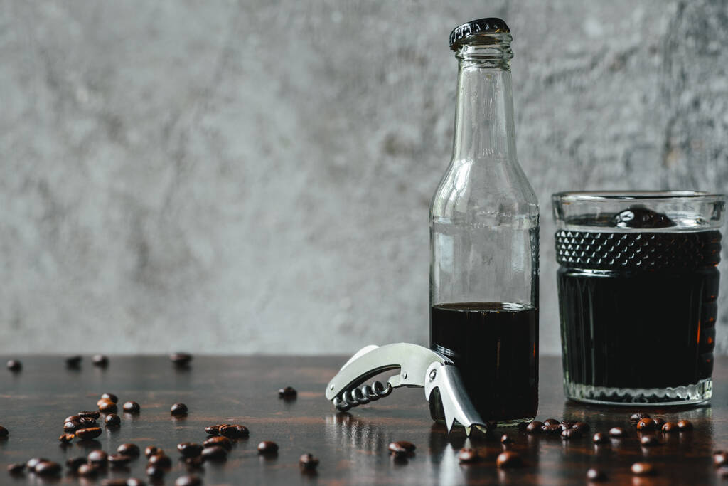 café cerveja fria em vidro e garrafa perto de abridor e grãos de café
 - Foto, Imagem
