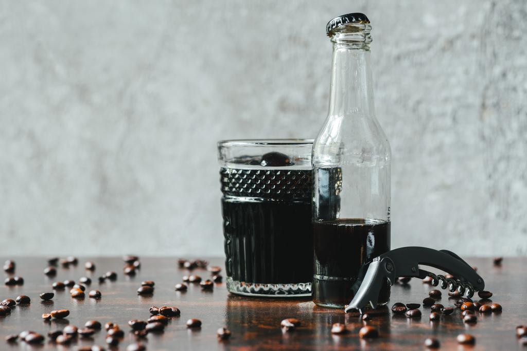 Холодный кофе в бутылке и стакане возле открывашки и кофейных зерен
 - Фото, изображение