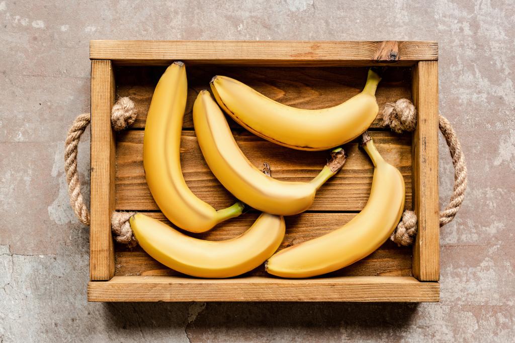 pohled shora na zralé banány v dřevěné krabici na ošlehaném povrchu - Fotografie, Obrázek