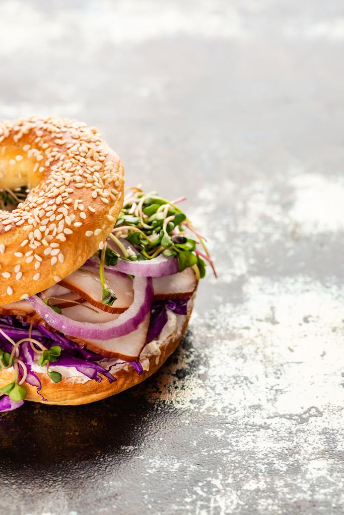 fresh delicious bagel with meat, red onion, cream cheese and sprouts on textured grey surface - Photo, Image