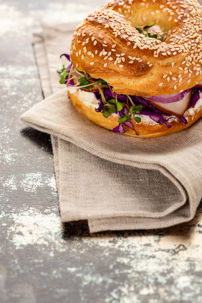 свежий вкусный бублик с мясом, красный лук, сливочный сыр и ростки на салфетке на текстурной поверхности
 - Фото, изображение