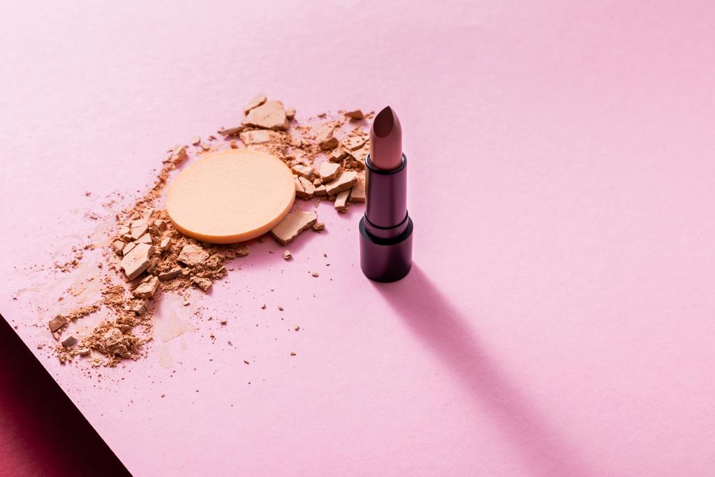 gebarsten gezicht poeder in de buurt van lippenstift en make-up spons op roze  - Foto, afbeelding