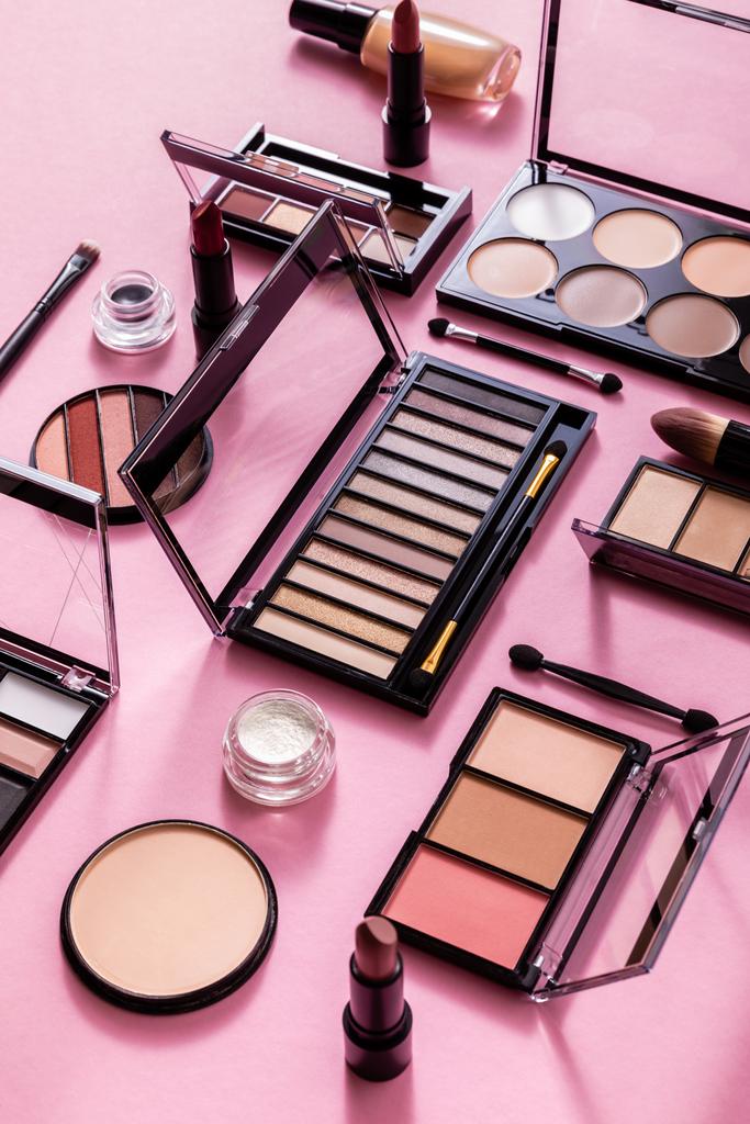 paletas de colorete y sombra de ojos cerca de cepillos cosméticos, base de la cara y lápiz labial en rosa
  - Foto, Imagen