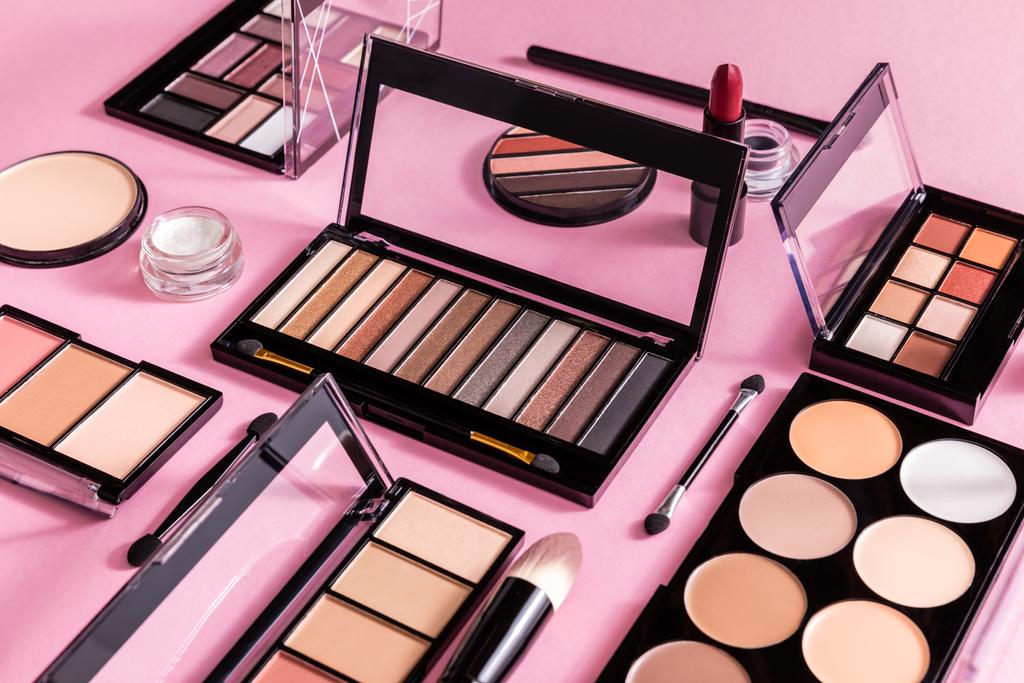 blush e paletas de sombra perto de escovas cosméticas e batom em rosa
  - Foto, Imagem