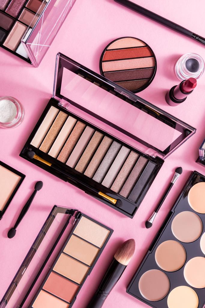 bovenaanzicht van lippenstift, cosmetische penselen en blozen in de buurt van oogschaduw palet op roze - Foto, afbeelding