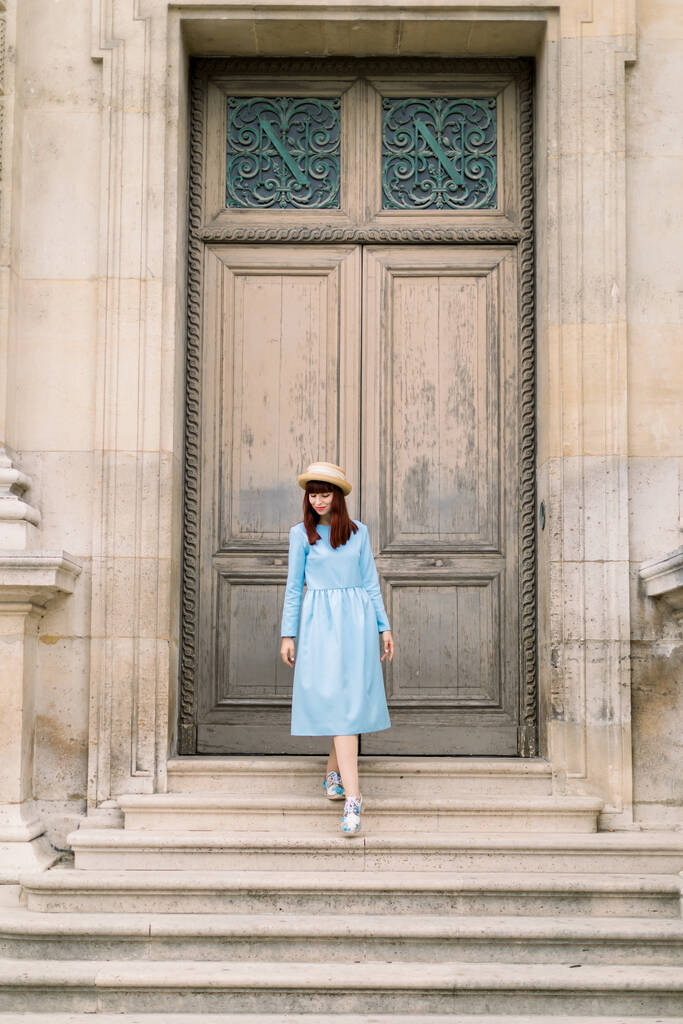 Foto einer schönen jungen Frau in blauem Kleid geht die Vintage-Treppe auf dem Hintergrund des alten Gebäudes mit Türen - Foto, Bild