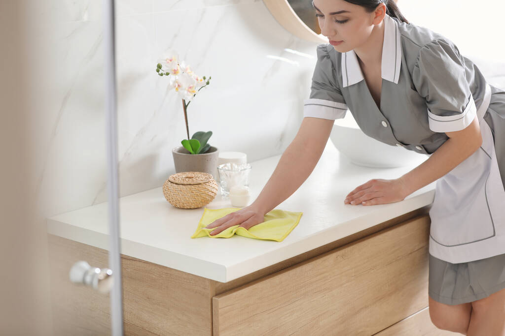 Jovem camareira limpando poeira da bancada no banheiro
 - Foto, Imagem