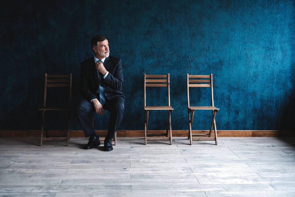 À espera de uma entrevista. Empresário maduro confiante sentado na cadeira contra fundo azul escuro
. - Foto, Imagem