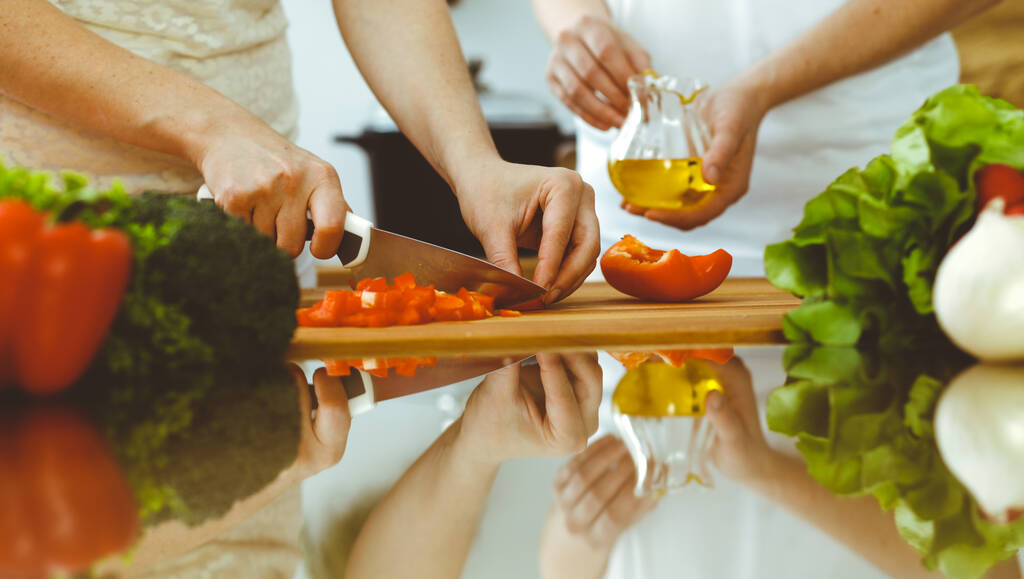 Detailní záběr lidských rukou vařících v kuchyni. Matka a dcera nebo dvě přítelkyně krájejí zeleninu na čerstvý salát. Přátelství, rodinná večeře a koncepce životního stylu - Fotografie, Obrázek