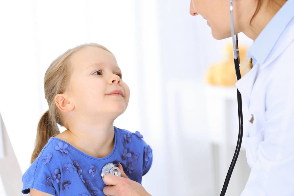 Lääkäri tutkii pikkutyttöä stetoskoopilla. Onnellinen hymyilevä lapsipotilas tavallisessa lääkärintarkastuksessa. Lääkkeiden ja terveydenhuollon käsitteet - Valokuva, kuva