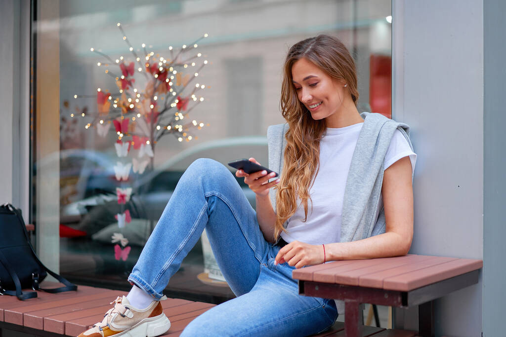 Nainen kaupunki katu kesä istuu penkki älypuhelin näyteikkuna ulkona Moderni tyylikäs matka tyttö reppu lepää onnellinen hymyilevä keski-ikä nainen yksin chattailuun matkapuhelin - Valokuva, kuva