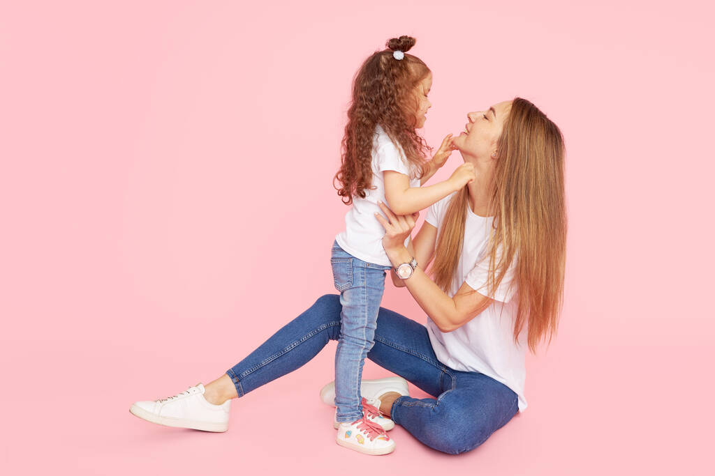 Valores familiares. Mãe e filha de camisetas brancas e jeans brincam e abraçam em um fundo rosa. Cuidar de entes queridos. Mãe feliz
 - Foto, Imagem