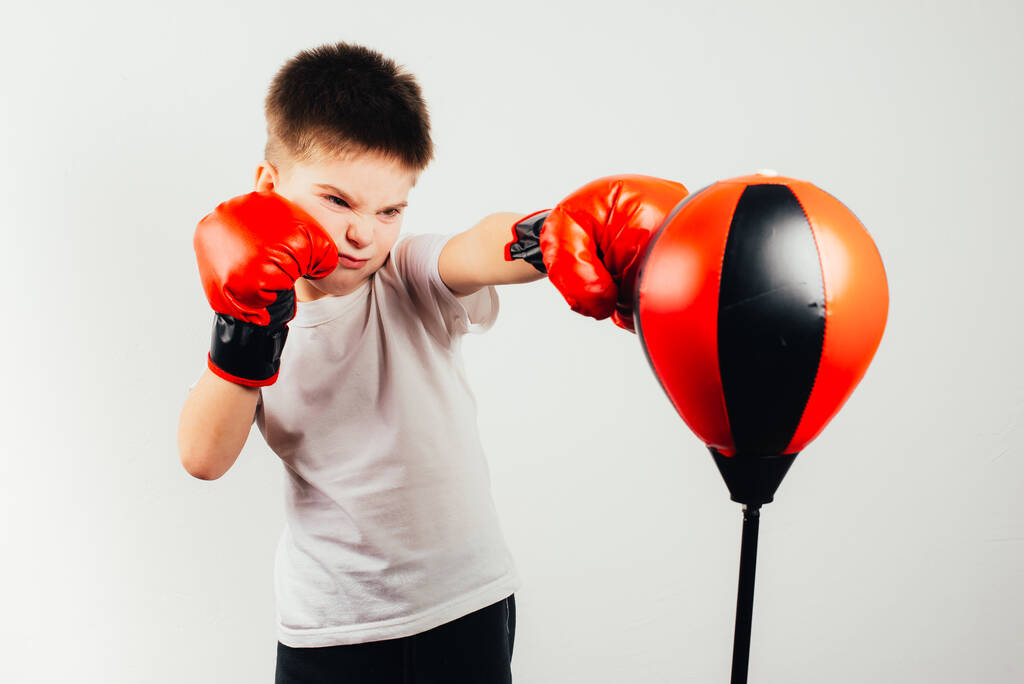 serious boy in boxing gloves training on grey background - Photo, Image