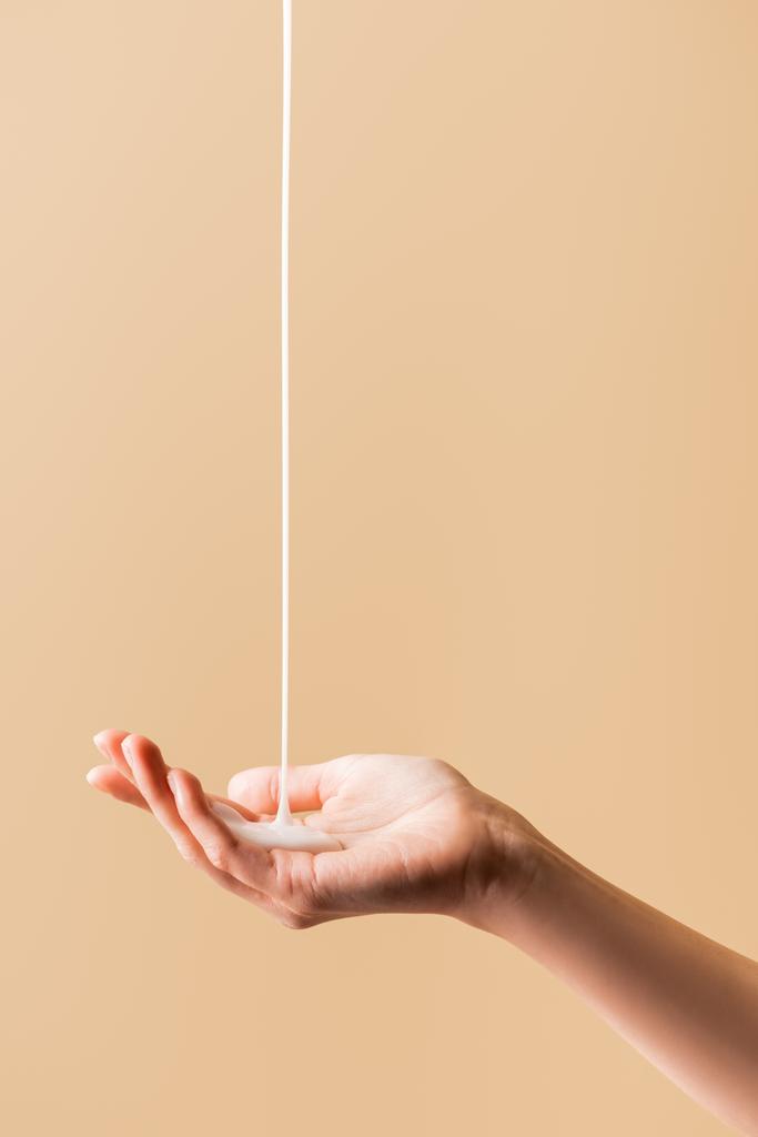 částečný pohled na ženskou ruku pod tekoucím tekutým mýdlem izolovaným na béžové - Fotografie, Obrázek