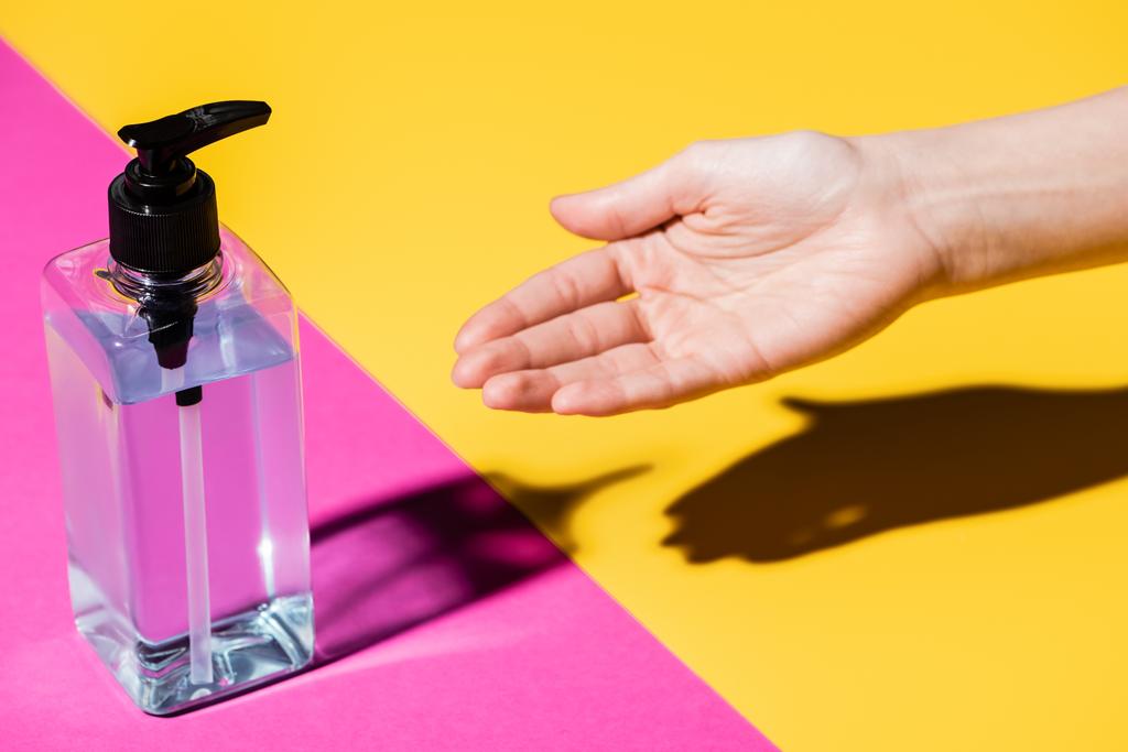 partial view of female hand near bottle with sanitizer on pink and yellow - Photo, Image