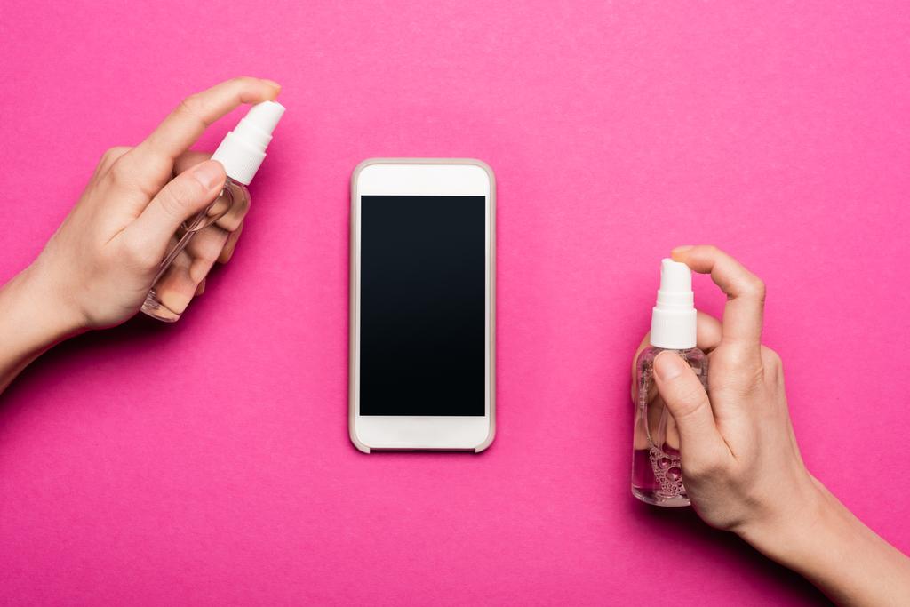 vista parcial de la mujer rociando antiséptico en el teléfono inteligente con pantalla en blanco en rosa
 - Foto, imagen