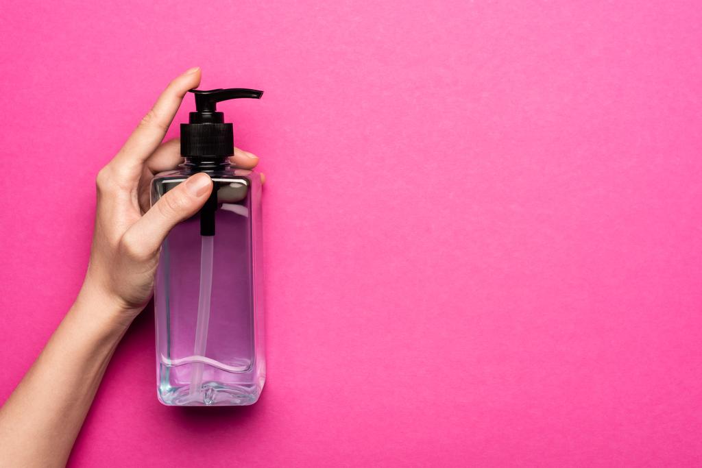 μερική άποψη της γυναίκας που κατέχουν μπουκάλι με αντισηπτικό σε ροζ - Φωτογραφία, εικόνα