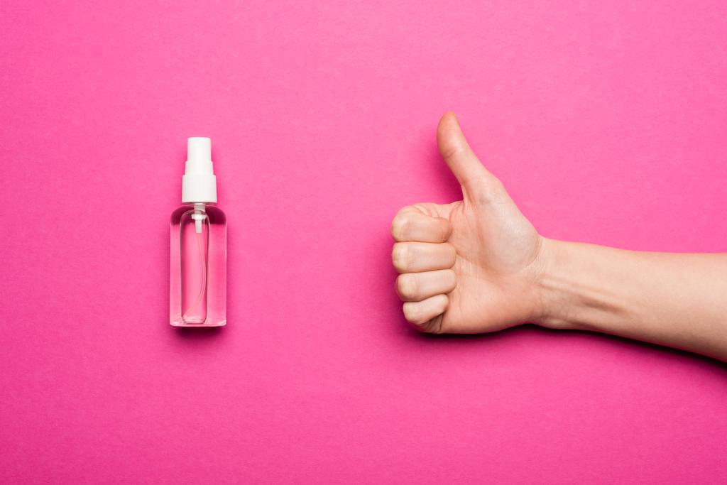 vista recortada de la mujer que muestra el pulgar hacia arriba cerca de la botella de aerosol con la mano antiséptico en rosa
 - Foto, Imagen