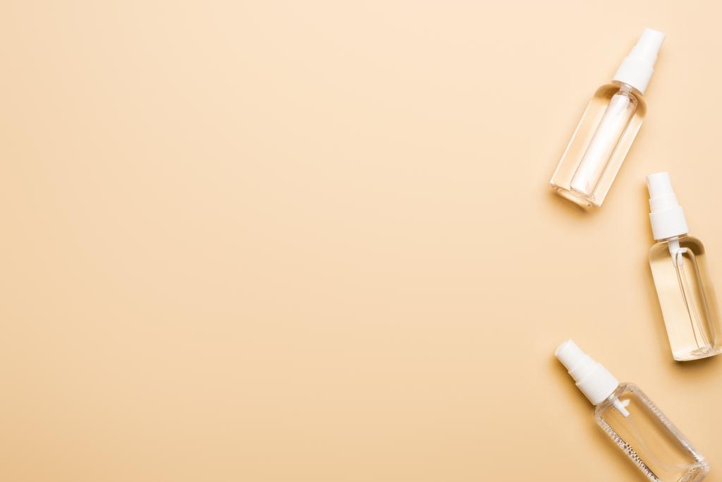bovenaanzicht van transparante spuitflessen met vloeibaar disifectiemiddel op beige - Foto, afbeelding
