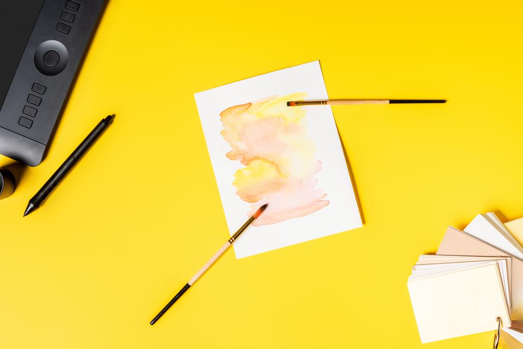 Stylus 'un yanında tablet, boya ve boya fırçaları ve sarı üzerine renk paleti çiziminin üst görünümü - Fotoğraf, Görsel