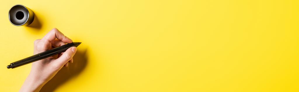 οριζόντια εικόνα του σχεδιαστή κρατώντας γραφίδα κοντά stylus κάτοχος σε κίτρινο  - Φωτογραφία, εικόνα