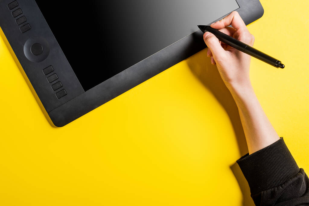 περικοπή άποψη του σχεδιαστή κρατώντας σύγχρονη γραφίδα κοντά στο σχέδιο δισκίο με λευκή οθόνη στο κίτρινο  - Φωτογραφία, εικόνα