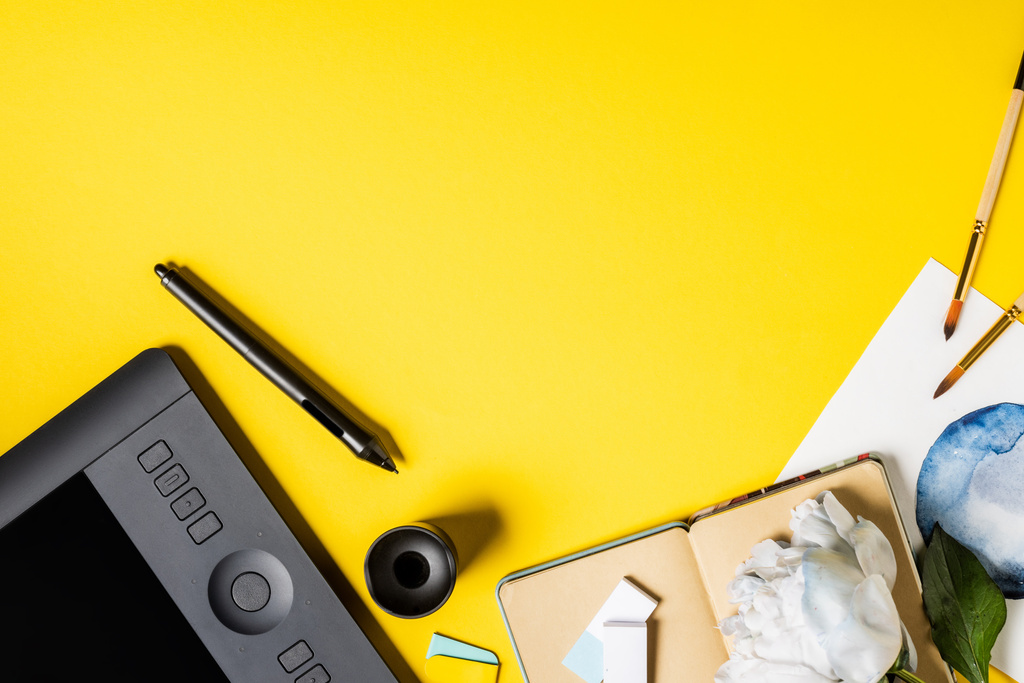 pohled shora na štětce v blízkosti malby, kreslicí tablet, stylus, zápisník a květ na žluté  - Fotografie, Obrázek