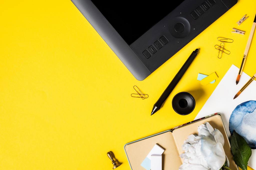 Ansicht von Malerei, Zeichentablette mit leerem Bildschirm, Clips, Stift, Notizbuch und Blume auf gelb  - Foto, Bild