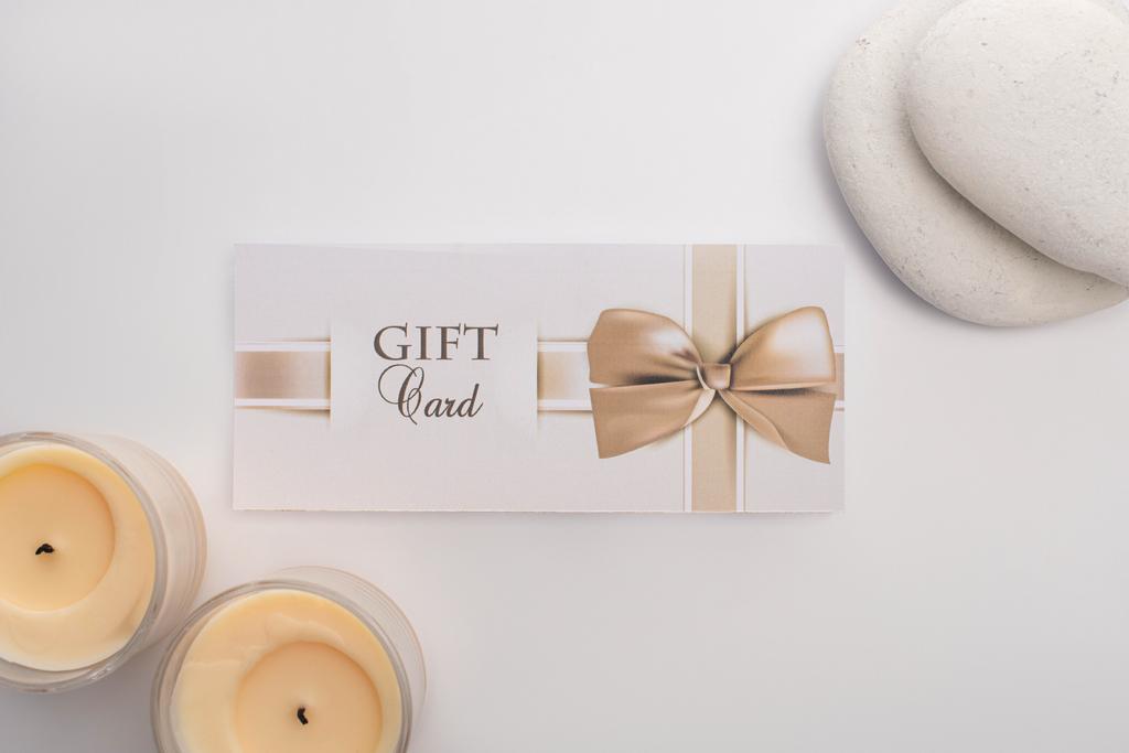 Κάτοψη της κάρτας δώρων κοντά σε κεριά και ζεν πέτρες σε λευκό φόντο - Φωτογραφία, εικόνα