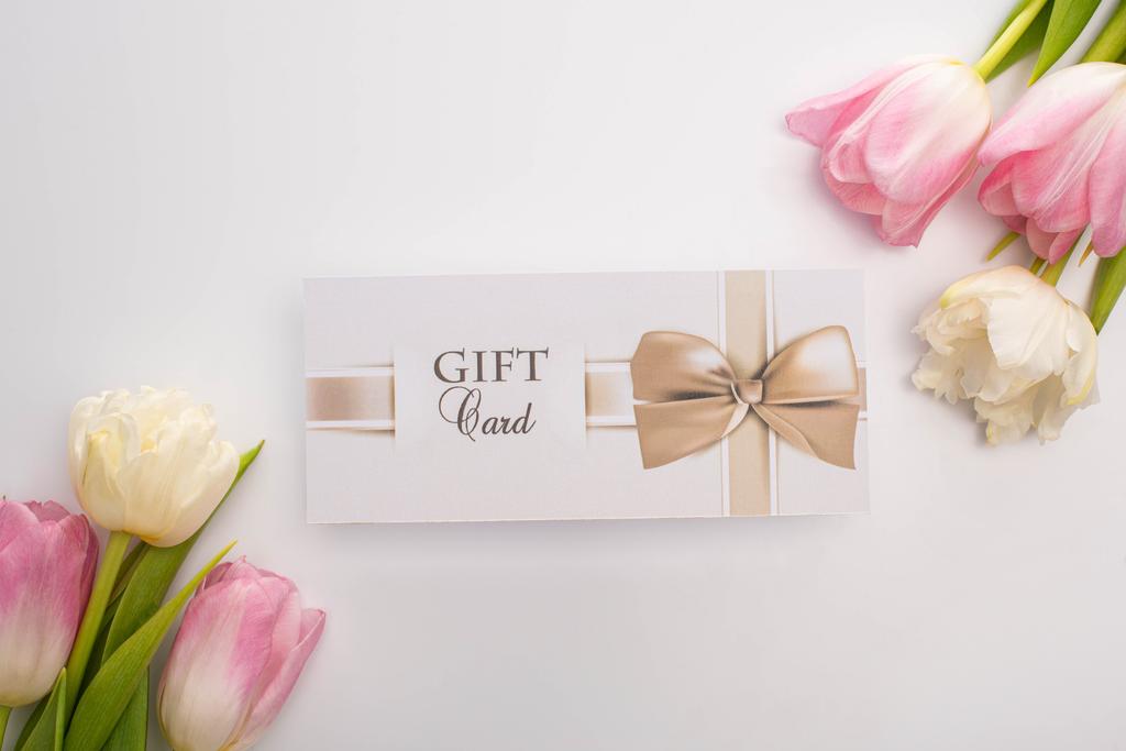 Draufsicht der Geschenkkarte in der Nähe von Tulpen auf weißem Hintergrund - Foto, Bild