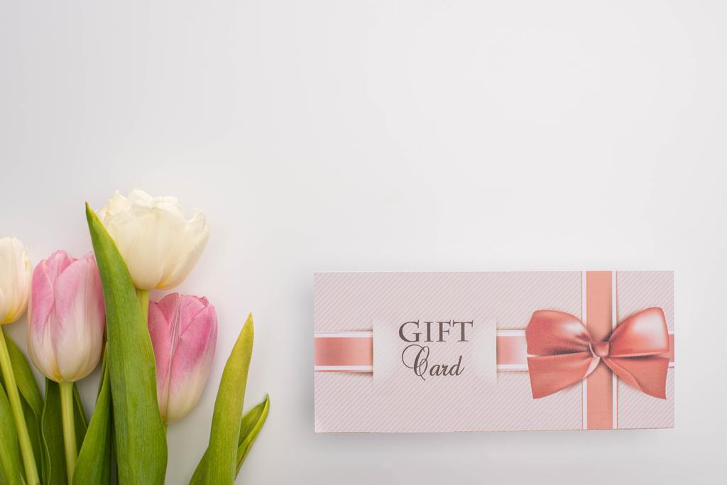 Bovenaanzicht van cadeaukaart met strik bij tulpen op witte achtergrond - Foto, afbeelding