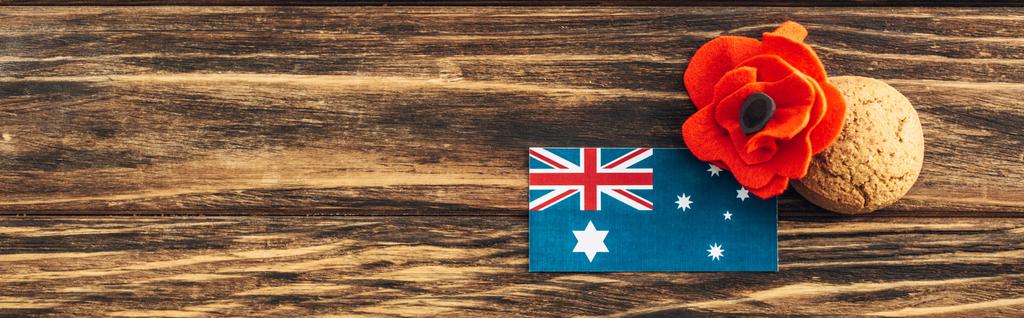 panoramisch gewas van Australische vlag in de buurt van kunstmatige bloem en koekje op houten oppervlak  - Foto, afbeelding