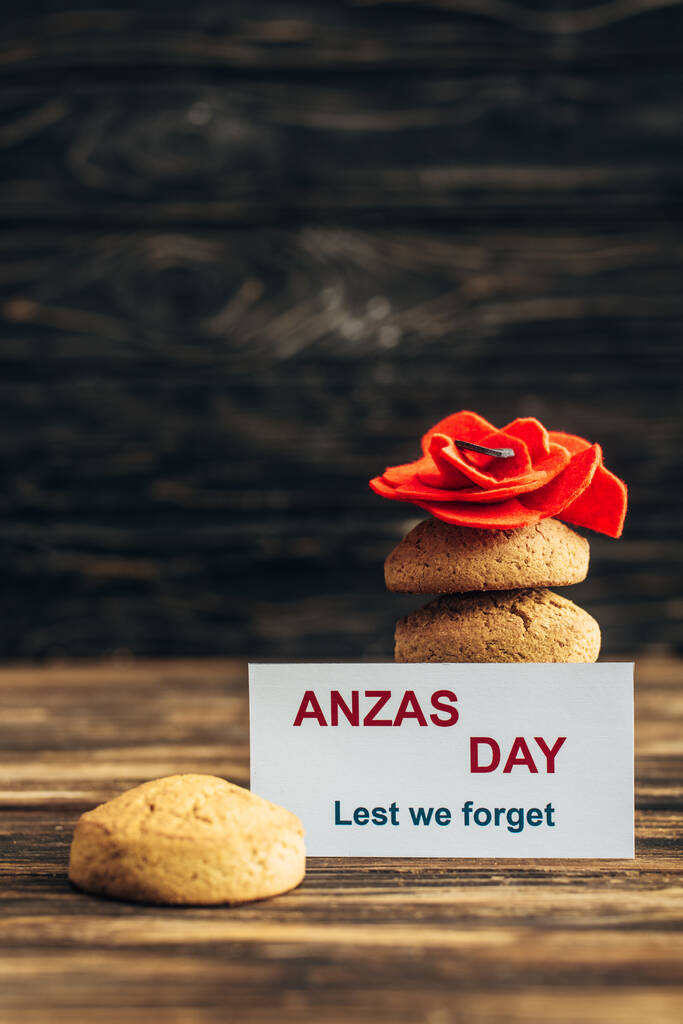 открытка с надписью "день анз" возле искусственного цветка и вкусным печеньем на деревянной поверхности
  - Фото, изображение