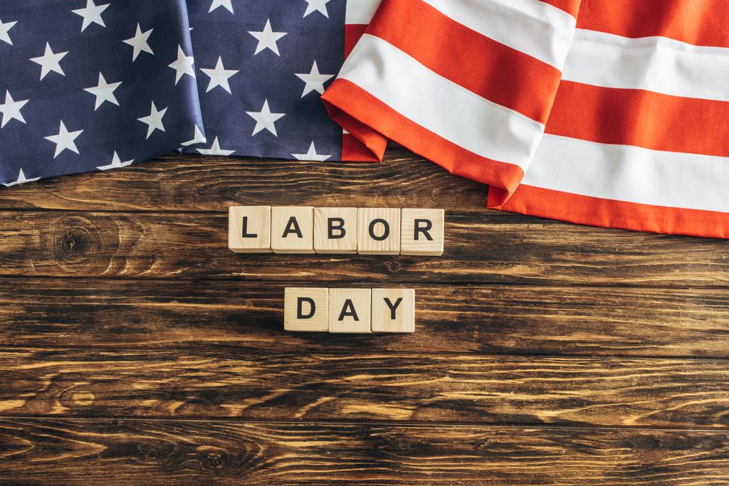 верхний вид американского флага со звездами и полосами возле кубов с надписью "День труда" на деревянной поверхности
  - Фото, изображение